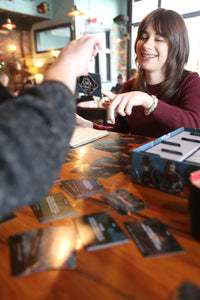 A woman enjoys coffee with a friend in a cafe, using Reckless Deck PSYCHE to fuel her creative writing process